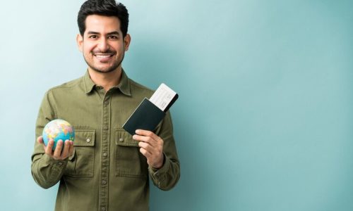 happy-young-man-holding-passport-boarding-pass-with-globe-while-standing-against-blue-background_662251-612