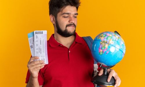 young-bearded-student-guy-red-polo-shirt-with-backpack-holding-globe-air-tickets-looking-intrigued-happy-standing-orange-background_141793-94126